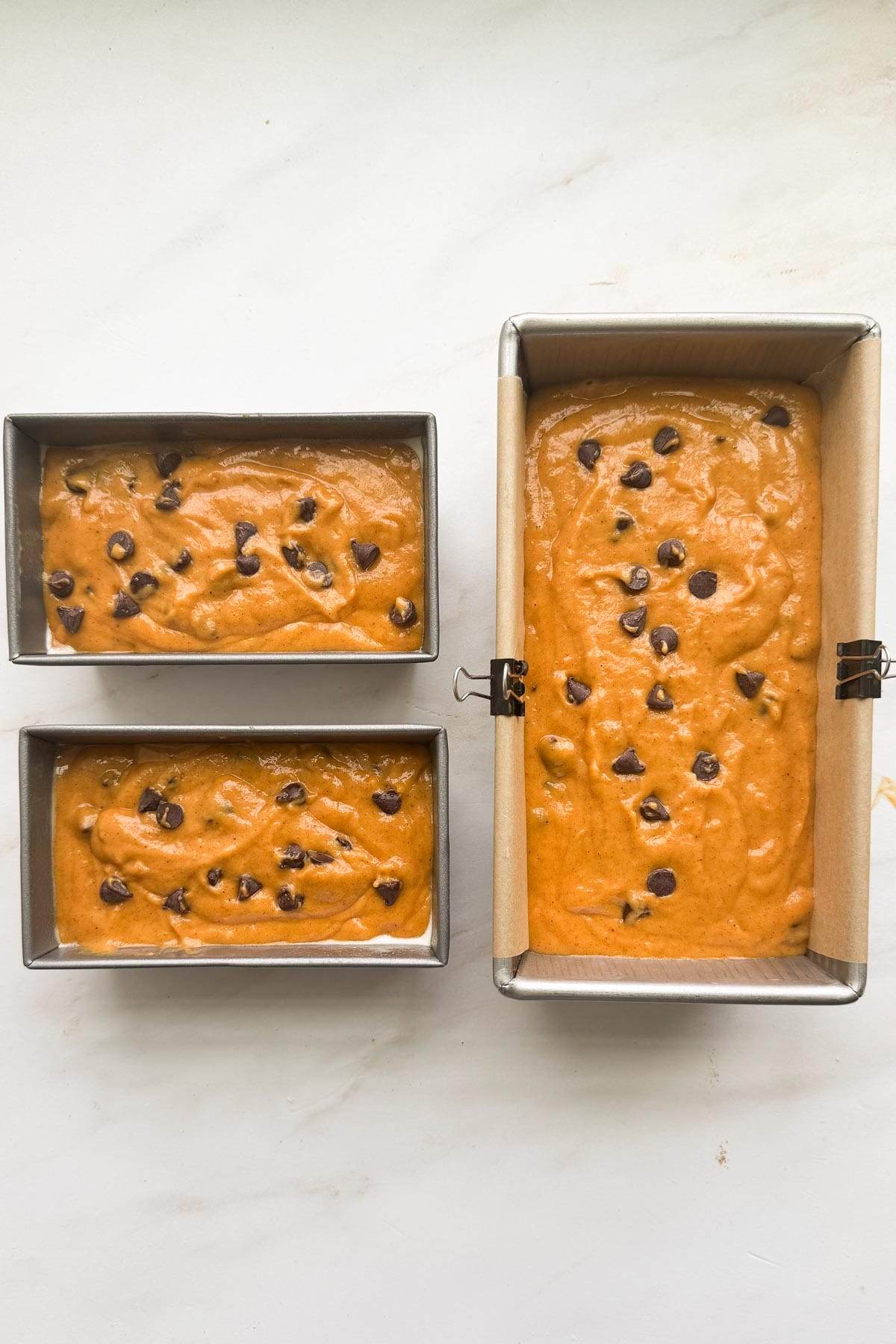 One large loaf pan and two mini loaf pans filled with chocolate chip pumpkin bread batter.