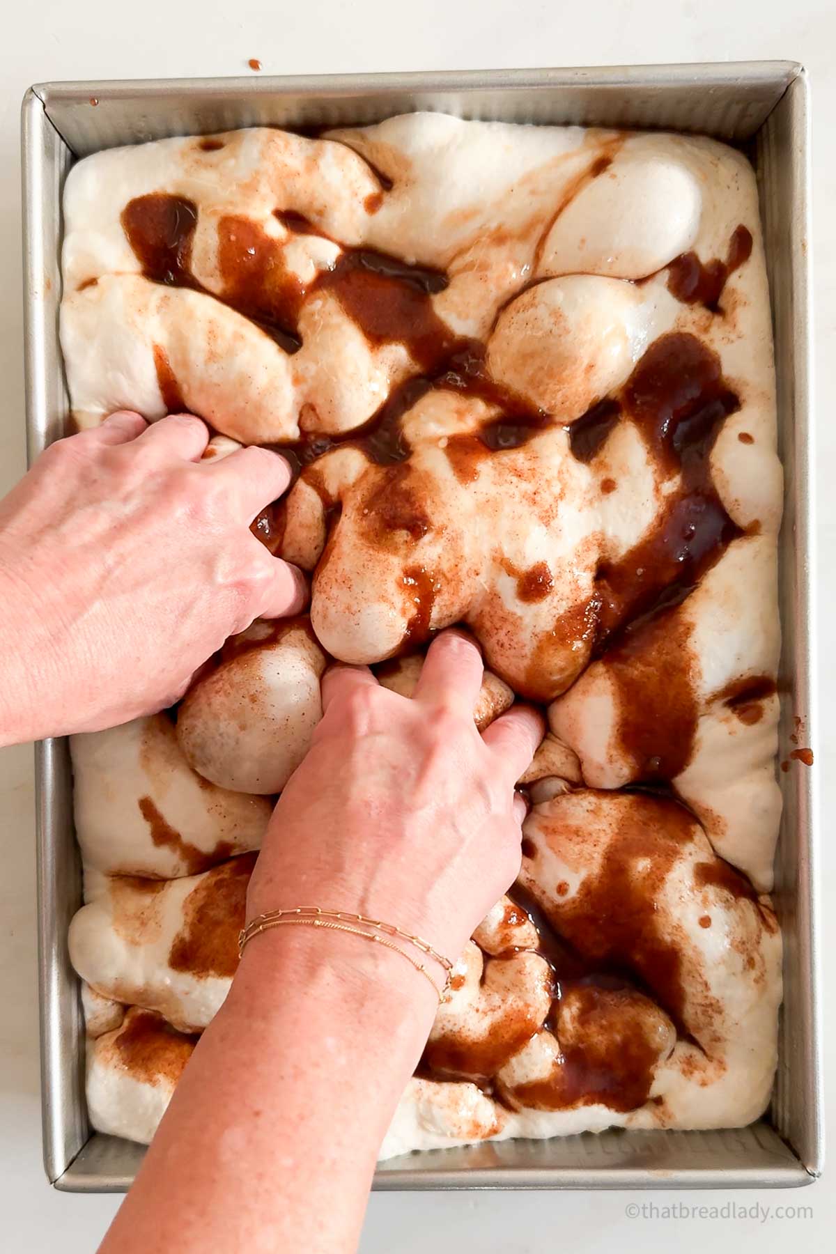 Hands dimpling cinnamon roll focaccia dough.