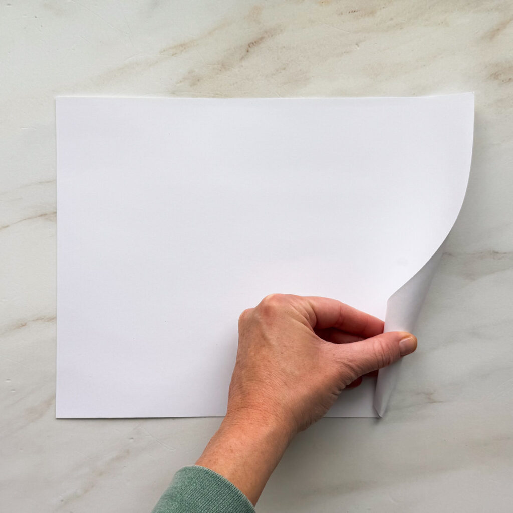 A hand rolling up a white 8.5 by 11-inch piece of paper.