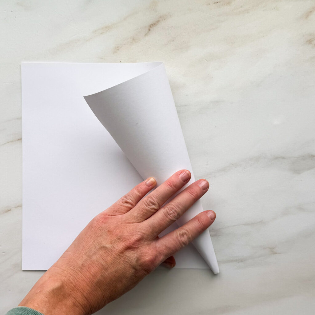 A hand rolling up a white 8.5 by 11-inch piece of paper.