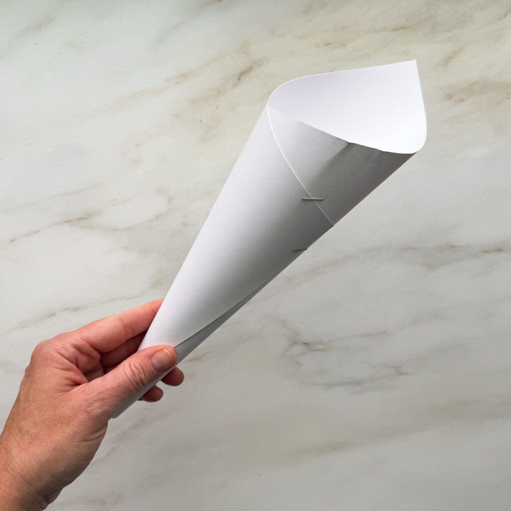 A white 8.5 by 11-inch piece of paper rolled up to a cone shape and stapled closed.