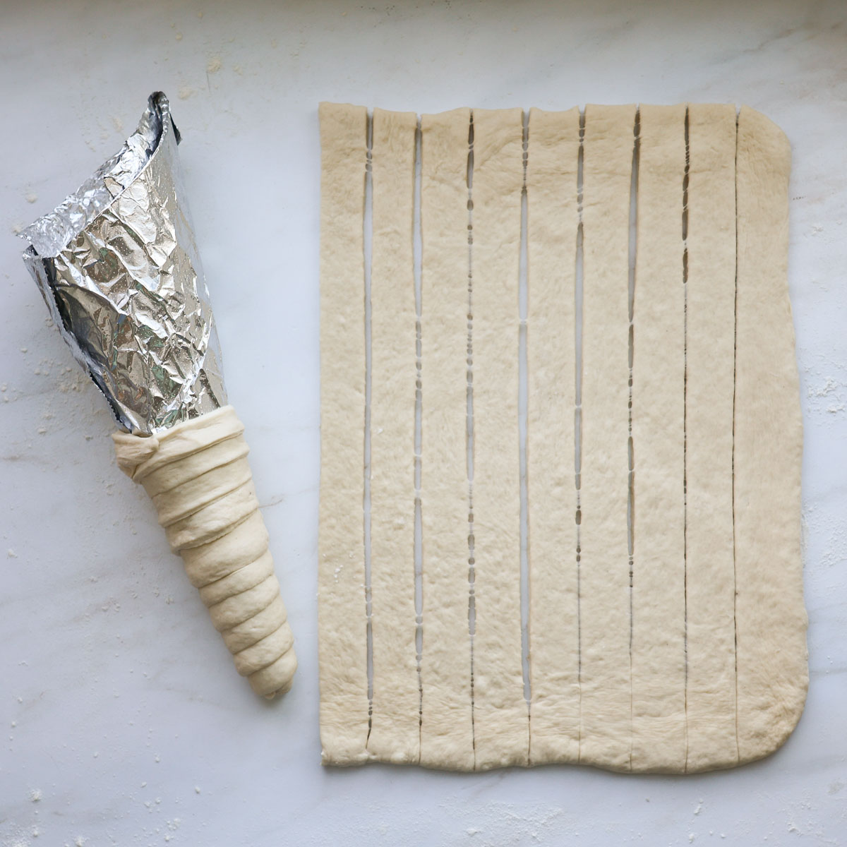 An aluminum cone mold with dough wrapped around it, laying on a countertop next to strips of dough.