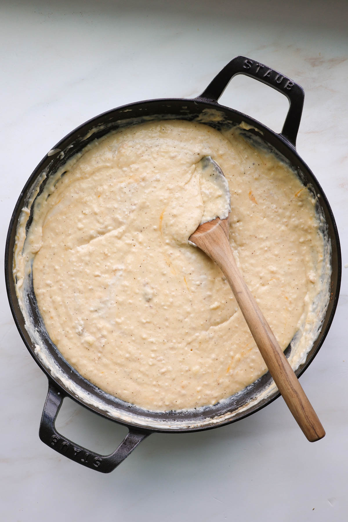 A cast iron pan with mac and cheese sauce with a wooden spoon.