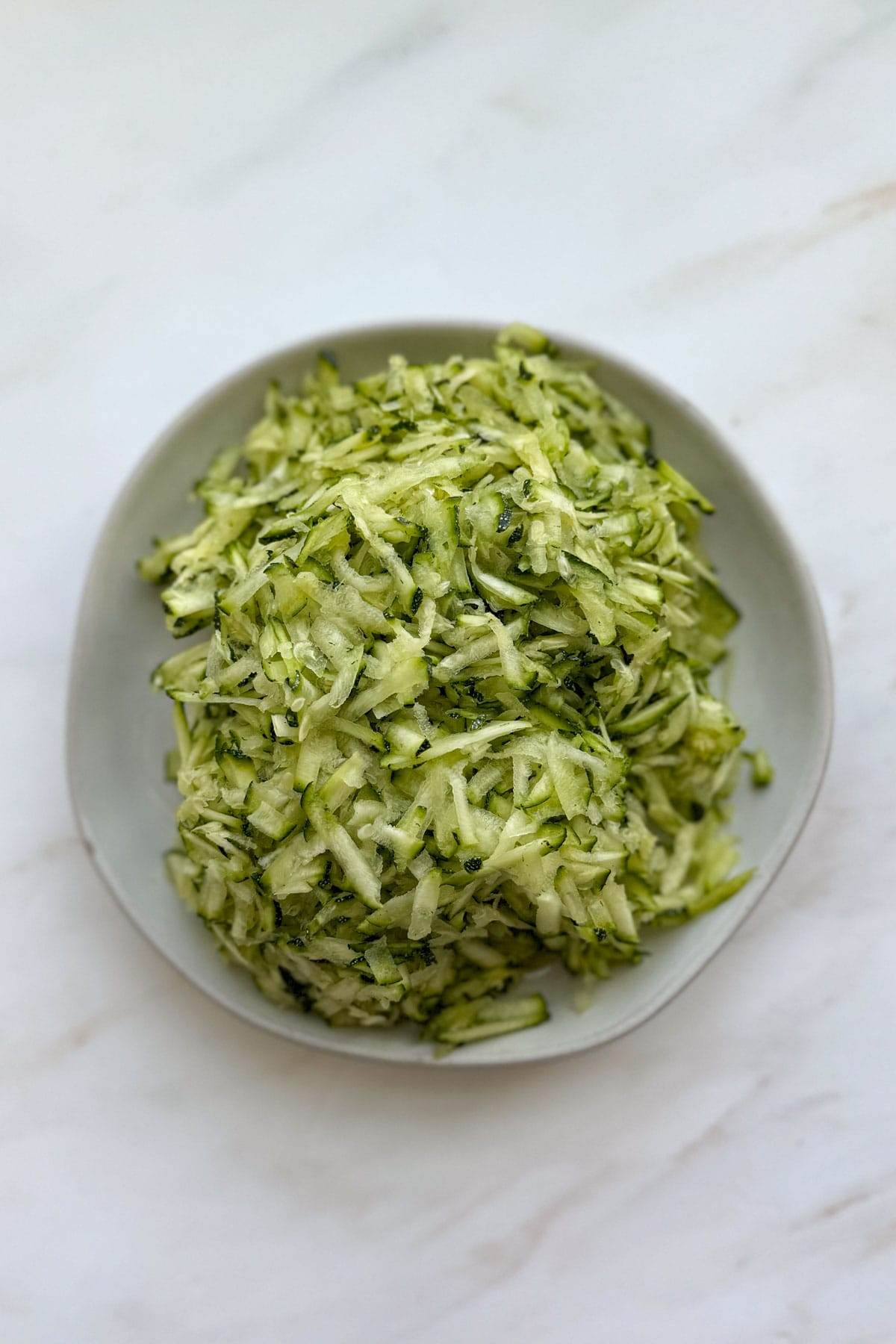A pile of shredded zucchini on a white plate.