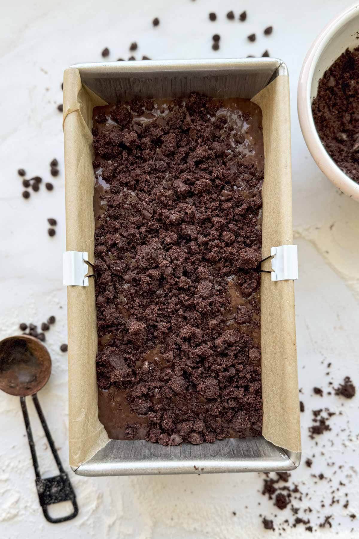 A parchment lined loaf pan filled with double chocolate zucchini bread batter and topped with chocolate streusel topping.