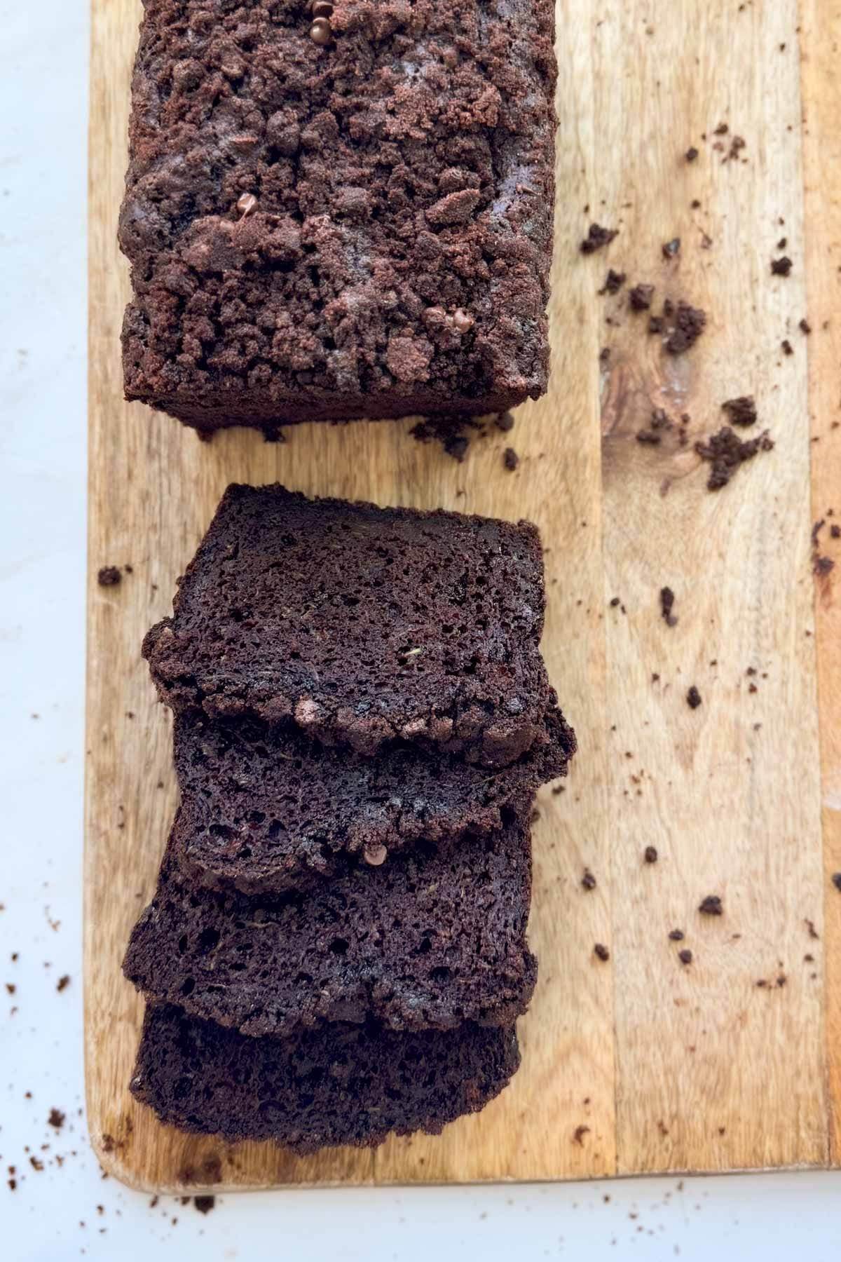 A loaf of double chocolate zucchini bread sliced on a wood cutting board.