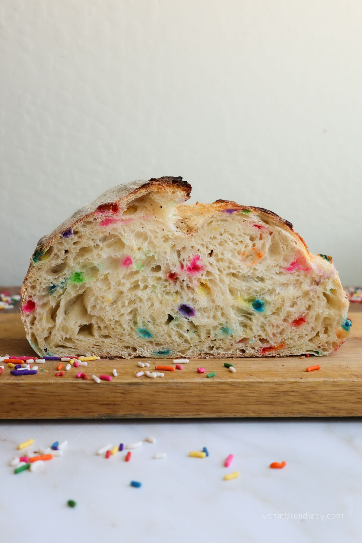 A cross-section of a funfetti sourdough loaf on a wood cutting board with sprinkles all around.
