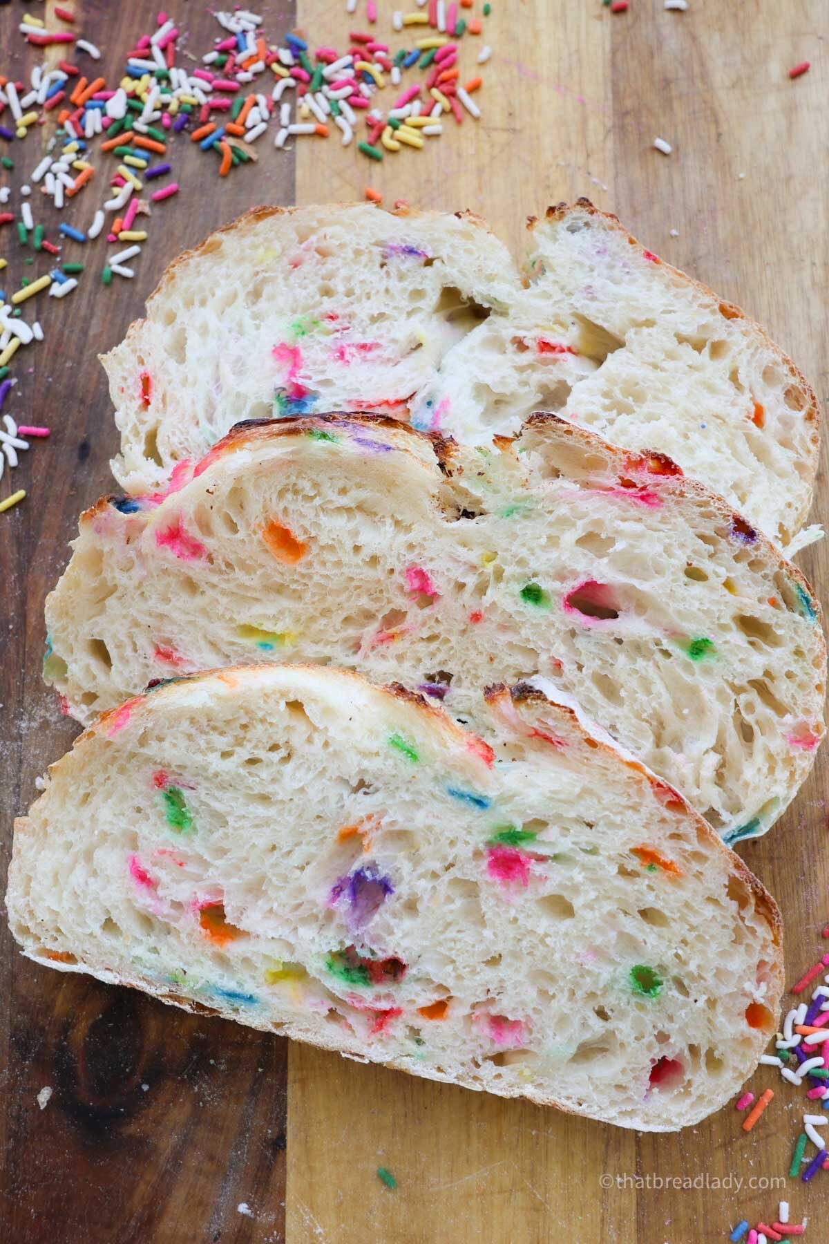 Three slices of funfetti sourdough on a wood cutting board with sprinkles around it.