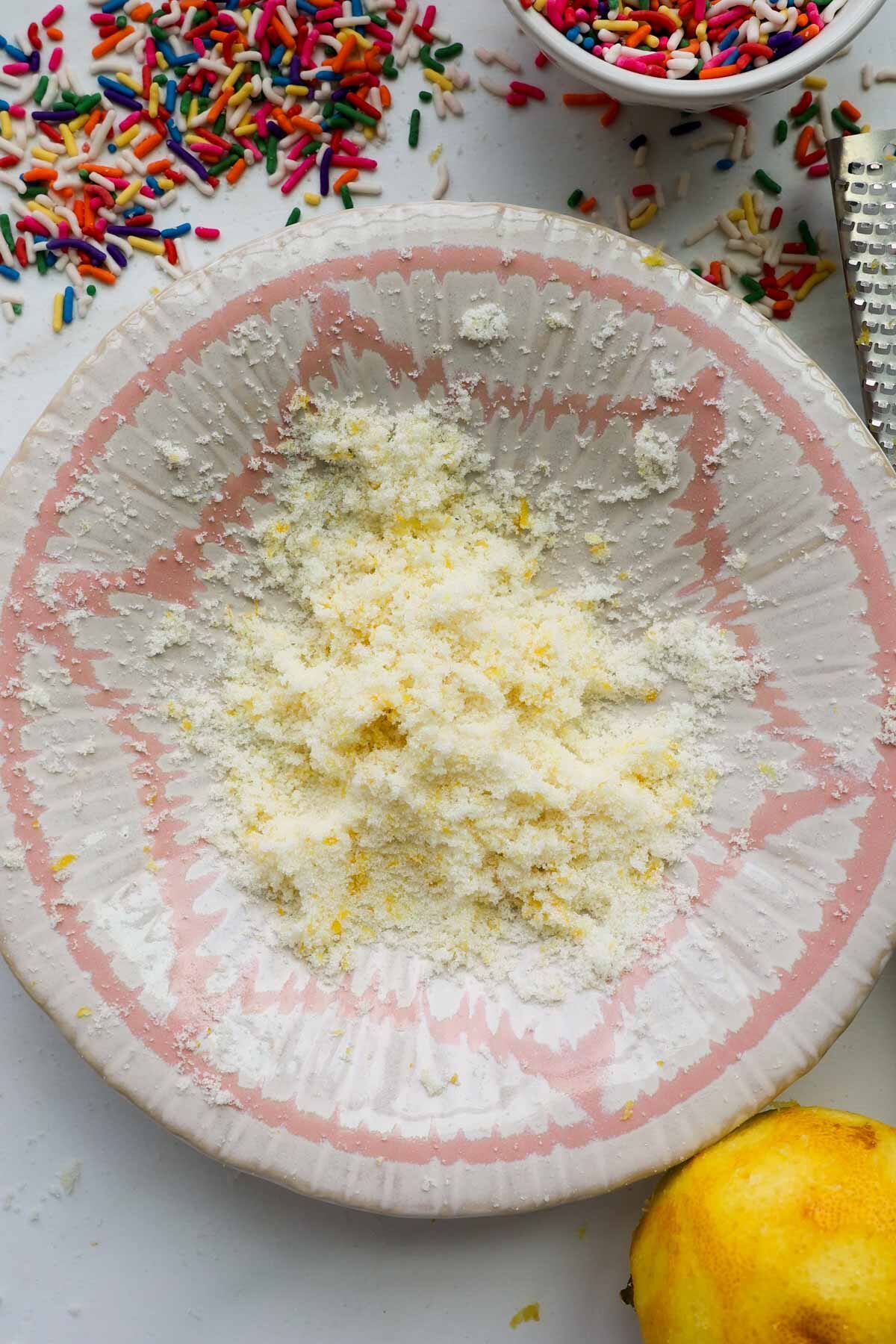 A bowl with lemon zest and sugar and sprinkles around it.