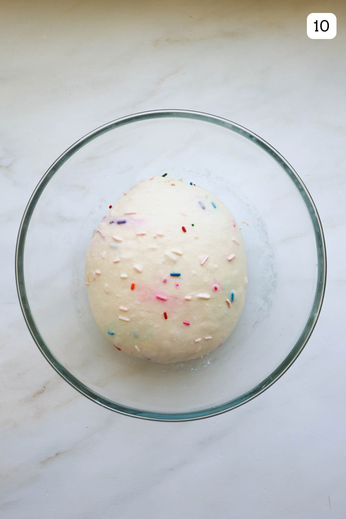 A glass bowl with a ball of dough with sprinkles throughout it.