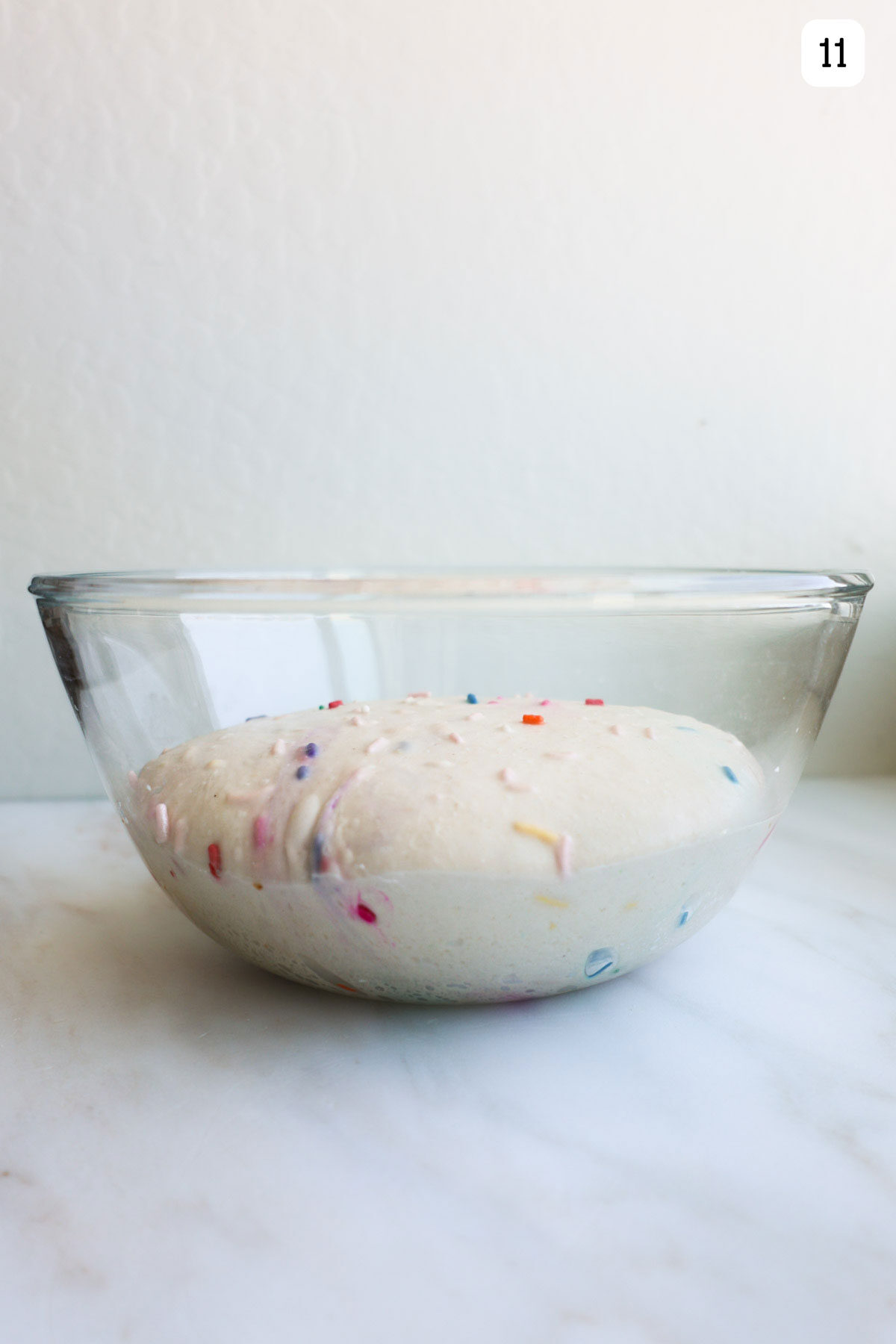 A glass bowl with risen bread dough with sprinkles in it.