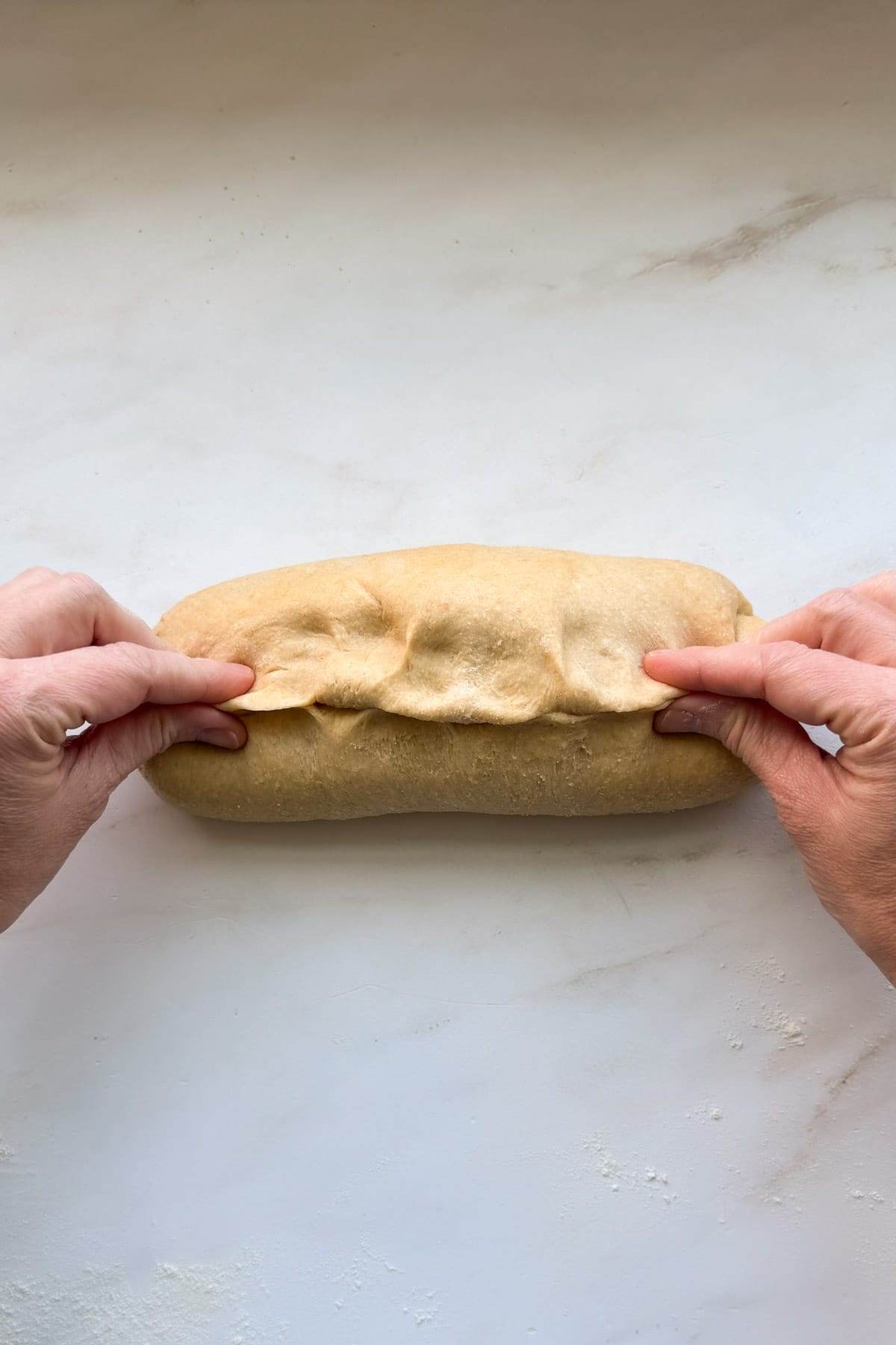 Two hands pinching the seam shut of the honey whole wheat bread loaf.