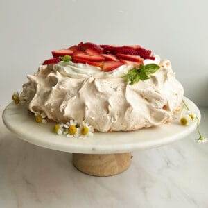 Pavlova on a platter topped with whipped cream and berries.