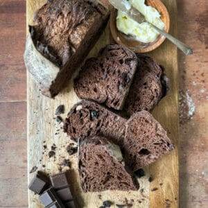 Sliced chocolate sourdough and butter on a cutting board.