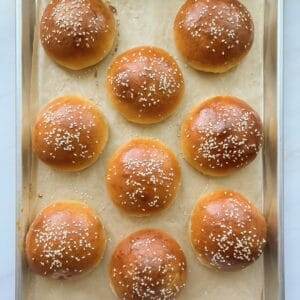 Nine hamburger buns on a baking sheet.
