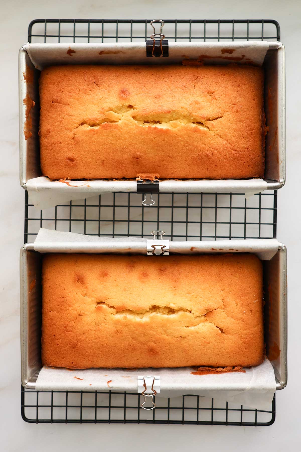 Two baked lemon coconut loaves in the pans on a cooling rack.