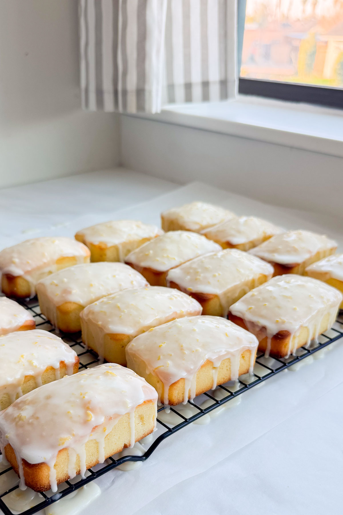 Several little loaves of lemon coconut bread on a cooling rack with the icing dripping down the sides.