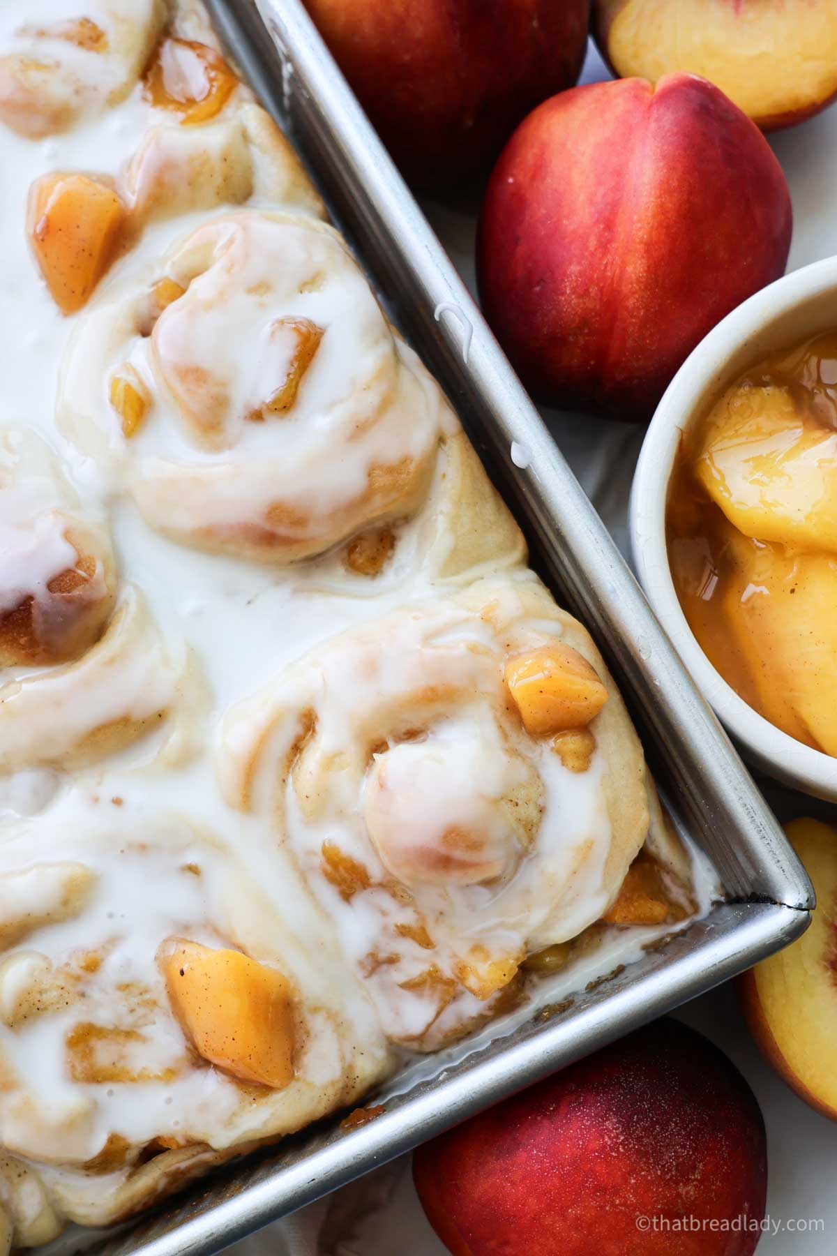 A pan of peach cinnamon rolls with peaches all around.