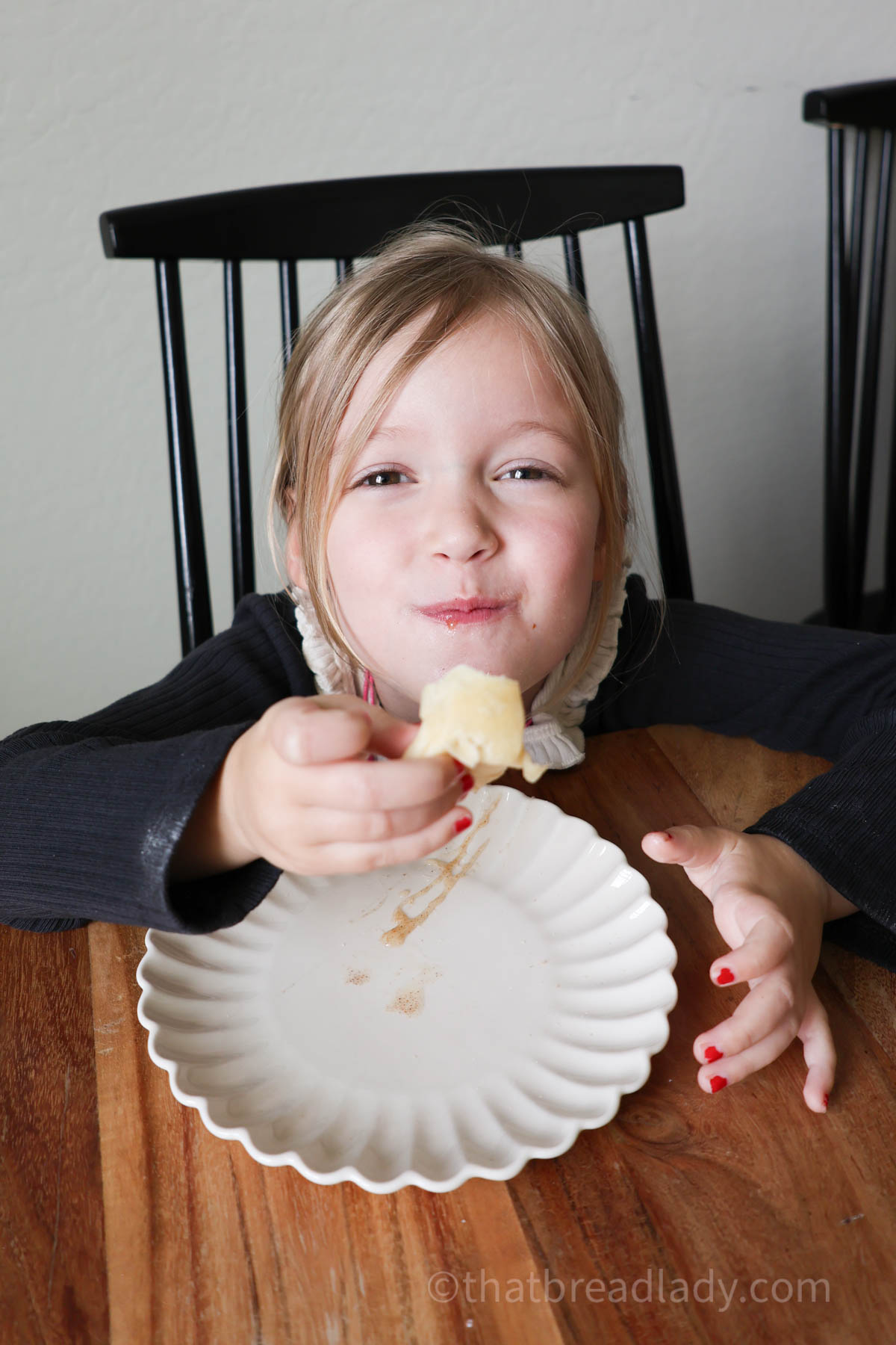 A little girl sitting at a table, smiling and eating a resurrection roll.
