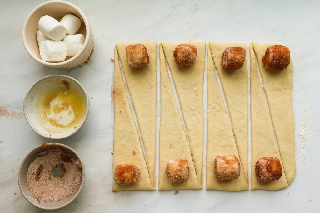 Cinnamon sugar marshmallows on triangles of roll dough with bowls of marshmallows, melted butter and cinnamon sugar on the side.
