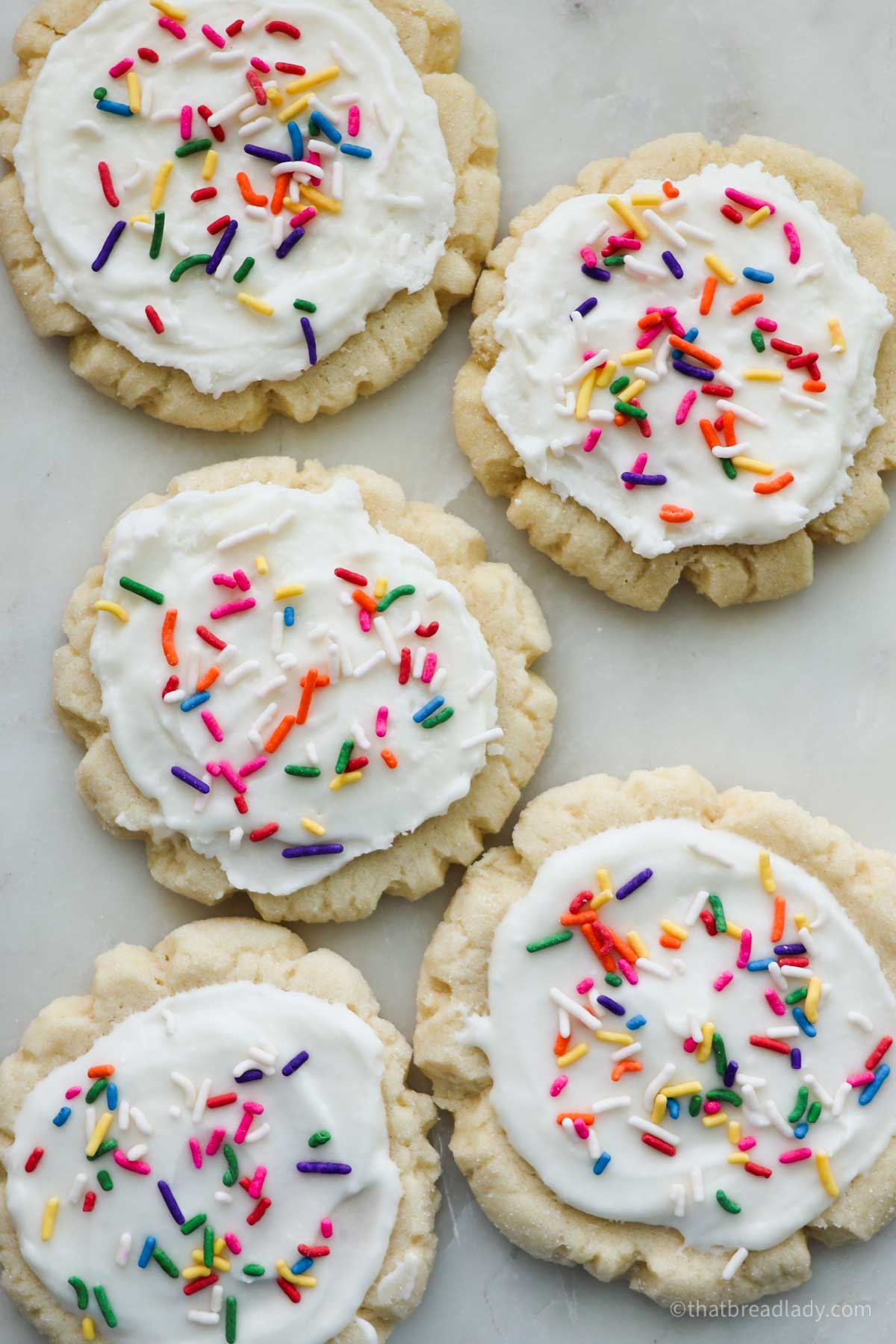 Several sourdough sugar cookies with white frosting and colorful sprinkles.
