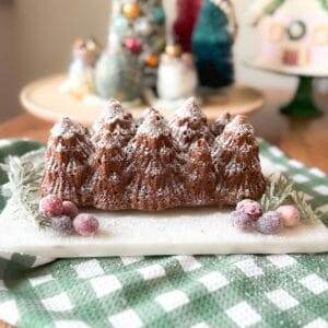 A loaf of spiced gingerbread on a green and white checked towel with Christmas decorations in the background.