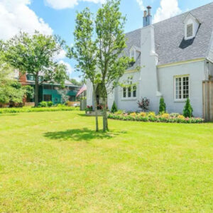 A cottage house with a yard of grass and trees.
