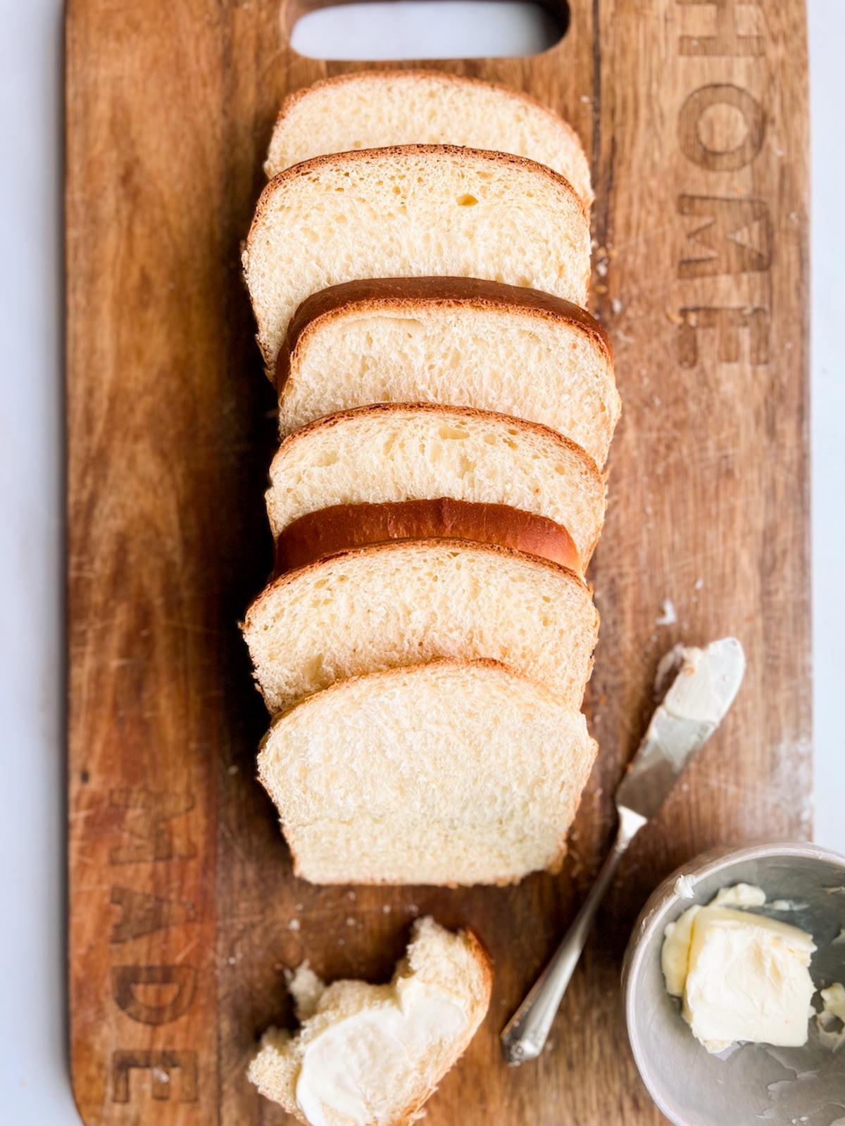 A loaf of sliced white bread on a wood cutting board.