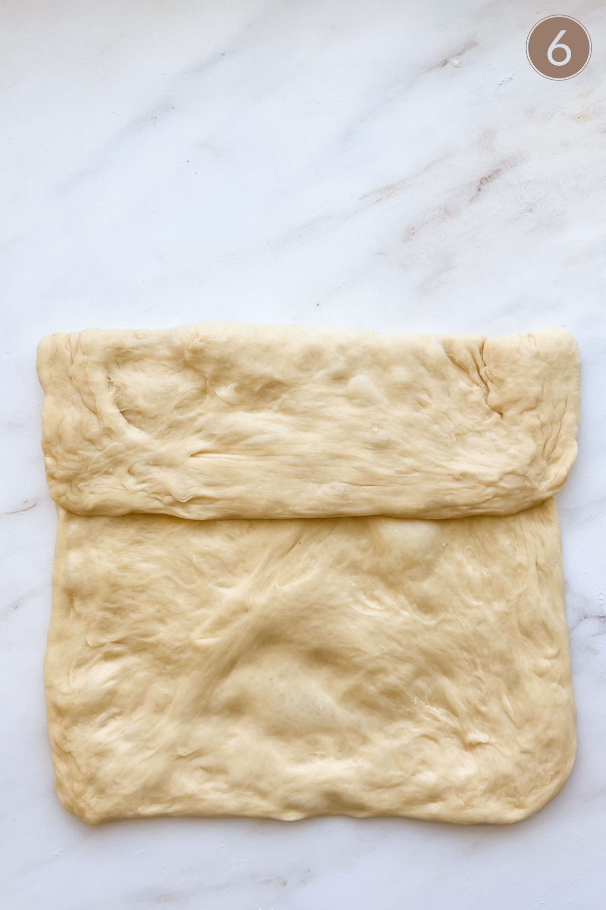 Bread dough flattened, with the top third folded over towards the center.