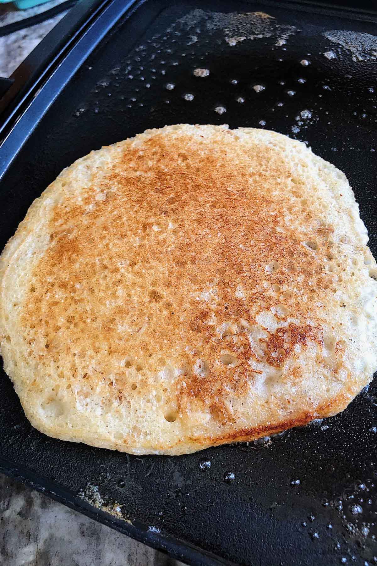 A whole wheat pancake on a buttered griddle.
