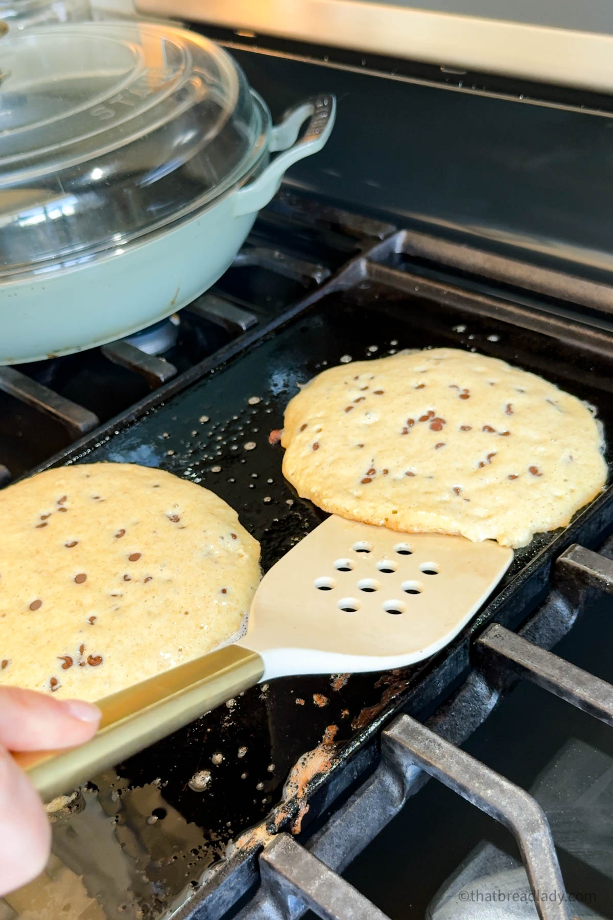 Two whole wheat chocolate chip pancakes on a buttered griddle.